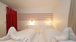 Hotellihuone, jossa on kaksi sänkyä, punaiset verhot ja raidallinen seinäkuvio.