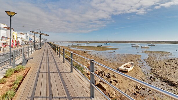 A wooden boardwalk leading to a beach with boats, a rocky shore, and a clear sky. - TAVIRA FORMOSA BAY 1 by HOMING (Cabanas de tavira)