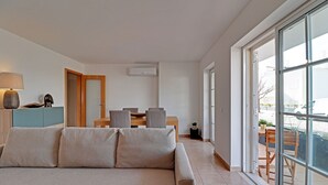 A modern living room with a sofa, a dining table with chairs, a lamp, and a sliding glass door leading to an outdoor area. - TAVIRA FORMOSA BAY 1 by HOMING (Cabanas de tavira)