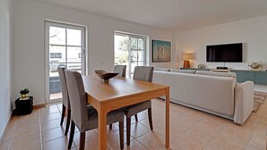 A modern living room with a dining table, sofa, and TV. - TAVIRA FORMOSA BAY 1 by HOMING (Cabanas de tavira)