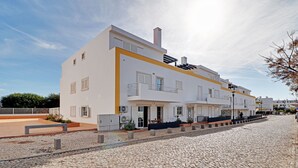 A modern building with a white facade and yellow accents, featuring balconies and a cobblestone street. - TAVIRA FORMOSA BAY 1 by HOMING (Cabanas de tavira)
