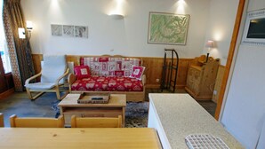 A cozy living room with a wooden sofa, a rocking chair, a wooden table, and a small kitchen area with a refrigerator. - Cozy apt 7 pers, lake view, Tignes (Tignes)