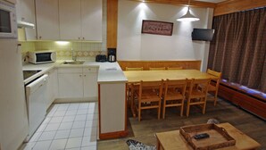 A compact kitchen with white cabinets, a microwave, a toaster, and a coffee maker. There's a wooden dining table with chairs, a TV mounted on the wall, and a patterned curtain. - Cozy apt 7 pers, lake view, Tignes (Tignes)