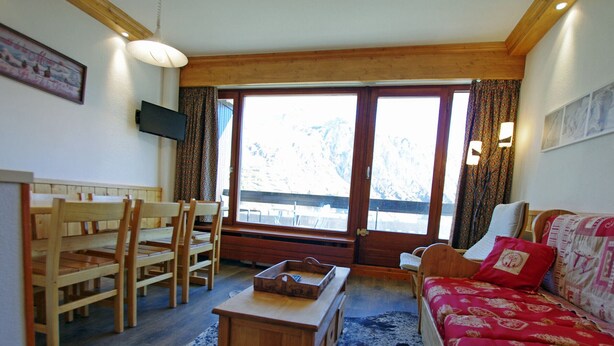 A cozy living room with a wooden sofa, a dining table with chairs, and a large window with curtains. - Cozy apt 7 pers, lake view, Tignes (Tignes)