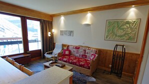 A cozy living room with a wooden floor, a red patterned sofa, a wooden coffee table, and a large window with curtains. - Cozy apt 7 pers, lake view, Tignes (Tignes)