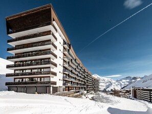 A multi-story hotel with balconies, set against a snowy mountainous backdrop.