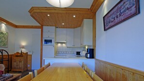 A dining area with a wooden table and chairs, a kitchen in the background, and a framed picture on the wall. - Cozy apt 7 pers, lake view, Tignes (Tignes)
