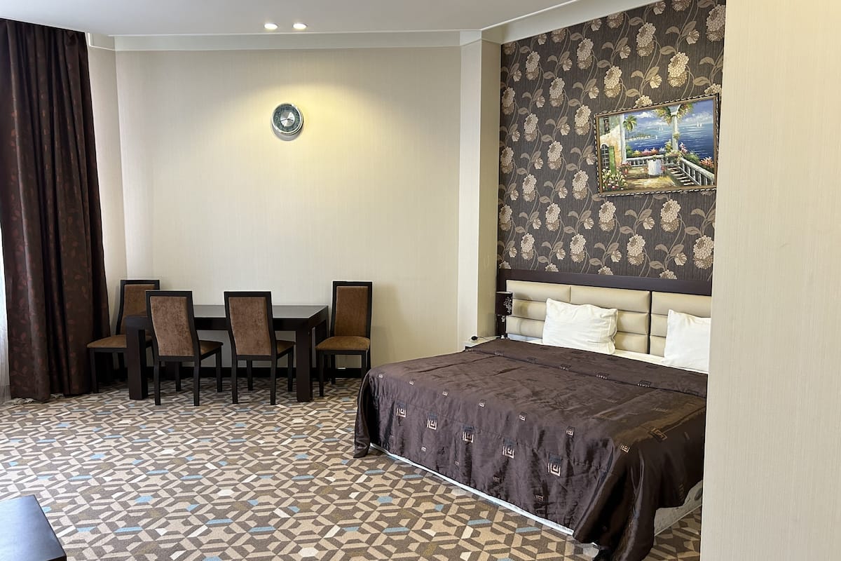 Ein Hotelzimmer mit einem Bett, einem Esstisch mit Stühlen, einer Wanduhr und floralem Wandpapier.