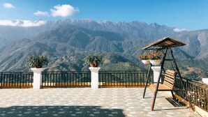 A terrace with a view of mountains, a wooden swing, and potted plants. - Muong Hoa View Hotel (Sa Pa)