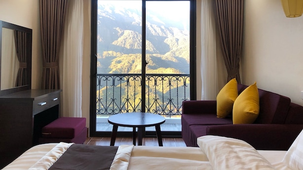 A hotel room with a bed, a sofa, a small table, and a TV. The room has a balcony with a mountain view. - Muong Hoa View Hotel (Sa Pa)