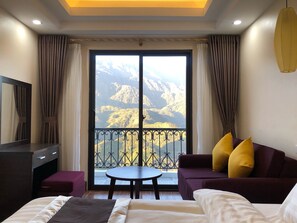 A hotel room with a bed, a sofa, a small table, and a TV. The room has a balcony with a mountain view. - Muong Hoa View Hotel (Sa Pa)