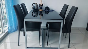 Ein moderner Essbereich mit einem Tisch mit Glasplatte, umgeben von schwarzen Stühlen, einer Kaffeekanne und einem kleinen dekorativen Gegenstand auf dem Tisch.