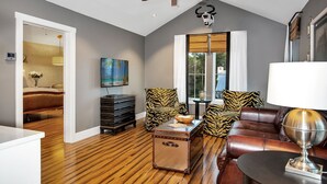 A modern living room with a ceiling fan, a large window with white curtains, a leather sofa, a tiger-print armchair, and a wooden coffee table. - Pecan Villa with Access to Swimming Pool and Hot Tub (Fredericksburg)