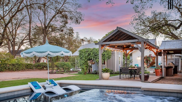 A backyard with a hot tub, lounge chairs, a pergola with string lights, and a covered patio area. - Pecan Villa with Access to Swimming Pool and Hot Tub (Fredericksburg)