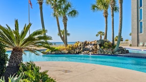 A swimming pool with palm trees and a view of the ocean. - Gulf-View King Bedroom | Beach Chairs Included | Long Beach Tower 3 (Panama City Beach)