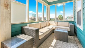 A sunroom with a large window, a beige sofa, wicker furniture, and a view of neighboring houses.