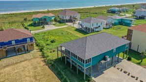 A coastal residential area with houses on stilts, a beach in the background, and a clear sky.