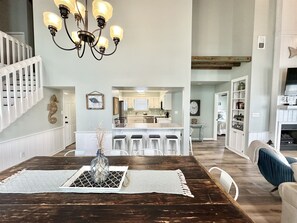 Enjoy meals in this dining area with a large table for four, a chandelier, and a kitchen nearby.