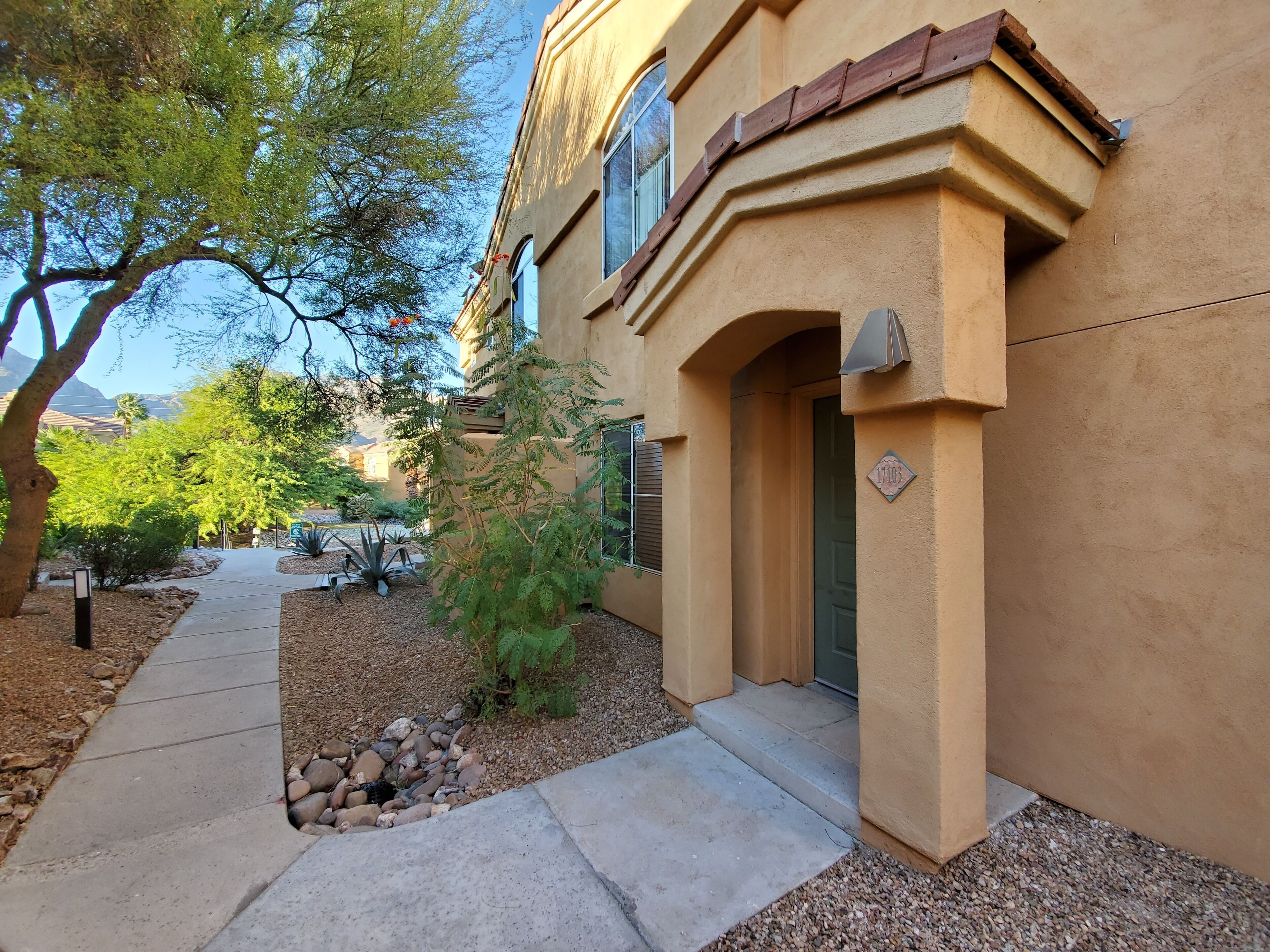 A building with a beige facade, a stone pathway, and a small garden with rocks and plants.