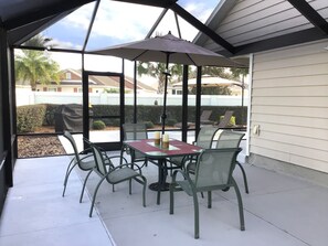 A covered patio with a table and chairs, a large umbrella, and a view of the neighborhood. - WOW! LOCATION! FUN! Includes HOT TUB, Gas Golf Cart, BBQ, & WIFI (The Villages)