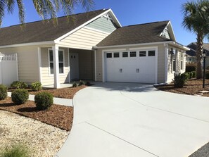 A single-story house with a garage, a covered porch, and a landscaped driveway. - WOW! LOCATION! FUN! Includes HOT TUB, Gas Golf Cart, BBQ, & WIFI (The Villages)