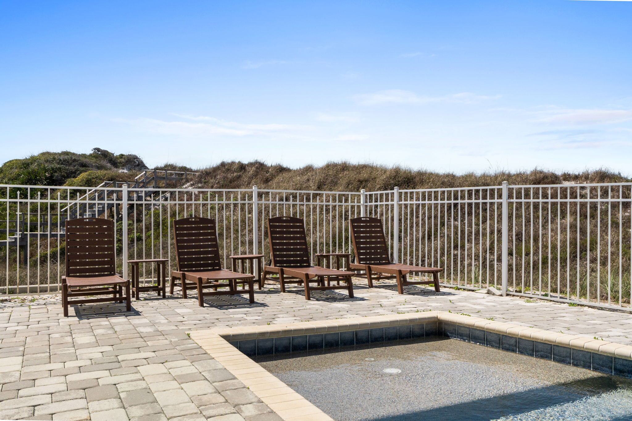 Un espace piscine avec des chaises longues et une petite piscine, le tout entouré d’une clôture et bordé, au fond, d’une colline verdoyante.