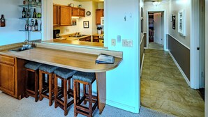 A kitchen with a bar area, wooden stools, and a view into the dining room. - Sugar Ski Comfort Unit 225 (Sugar Mountain)