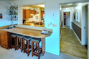 A kitchen with a bar area, wooden stools, and a view into the dining room.