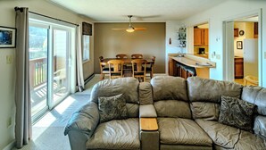 A living room with a large sectional sofa, a dining table with chairs, and a kitchen area visible through an open doorway. - Sugar Ski Comfort Unit 225 (Sugar Mountain)