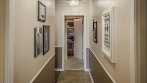 A hallway with framed artwork on the walls, a double black diamond caution sign, and a door leading to a room with a bed. - Sugar Ski Comfort Unit 225 (Sugar Mountain)