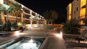 A pool area with lounge chairs, a hot tub, and a building with balconies.