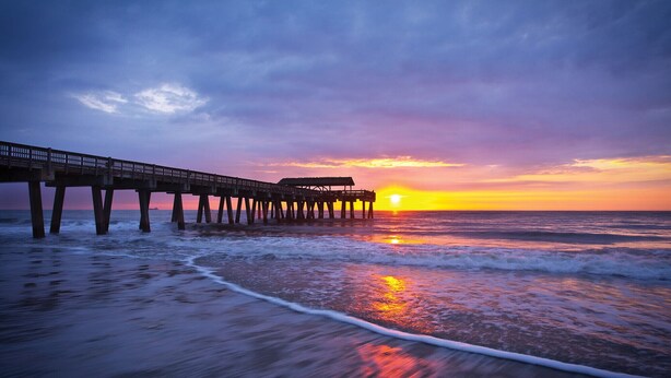 A pier extending into the ocean at sunset with waves crashing onto the shore.