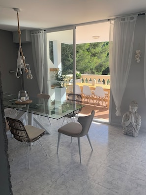 A modern dining area with a glass table, white chairs, and a view of a balcony with outdoor furniture. - Luxury Villa Felicidad with private pool, <br>5 double rooms, 4 bathrooms and sea views (Capdepera)