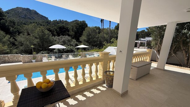 A balcony with a pool, white umbrellas, and a mountain view.