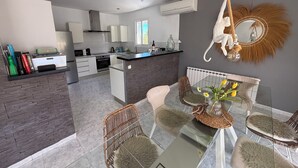A modern kitchen with white cabinets, a central island, and a dining area with a glass table and wicker chairs.