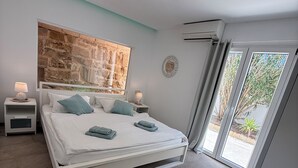 A modern bedroom with a bed, nightstands, a stone accent wall, and a view through a glass door.