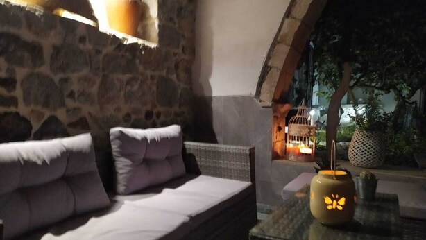 An outdoor seating area with a stone wall, cushioned seating, and a table with a lantern. - Romantic studio, city center, near beach, next market  and restaurants (Kalymnos)