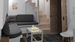 A loft-style room with a high ceiling, a built-in bed, a gray sofa, a small table with candles, a patterned rug, and a staircase leading to an upper level. - Romantic studio, city center, near beach, next market  and restaurants (Kalymnos)
