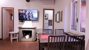 A living room with a fireplace, a television mounted on the wall, and a dining area with chairs and a table.