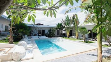 A swimming pool surrounded by white lounge chairs, a concrete deck, and tropical plants.