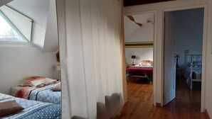 Ein Schlafzimmer mit Holzboden, einem Bett mit gemusterten Betttextilien, einem Nachttisch mit Lampe und einem Fenster mit Blick zum Himmel.