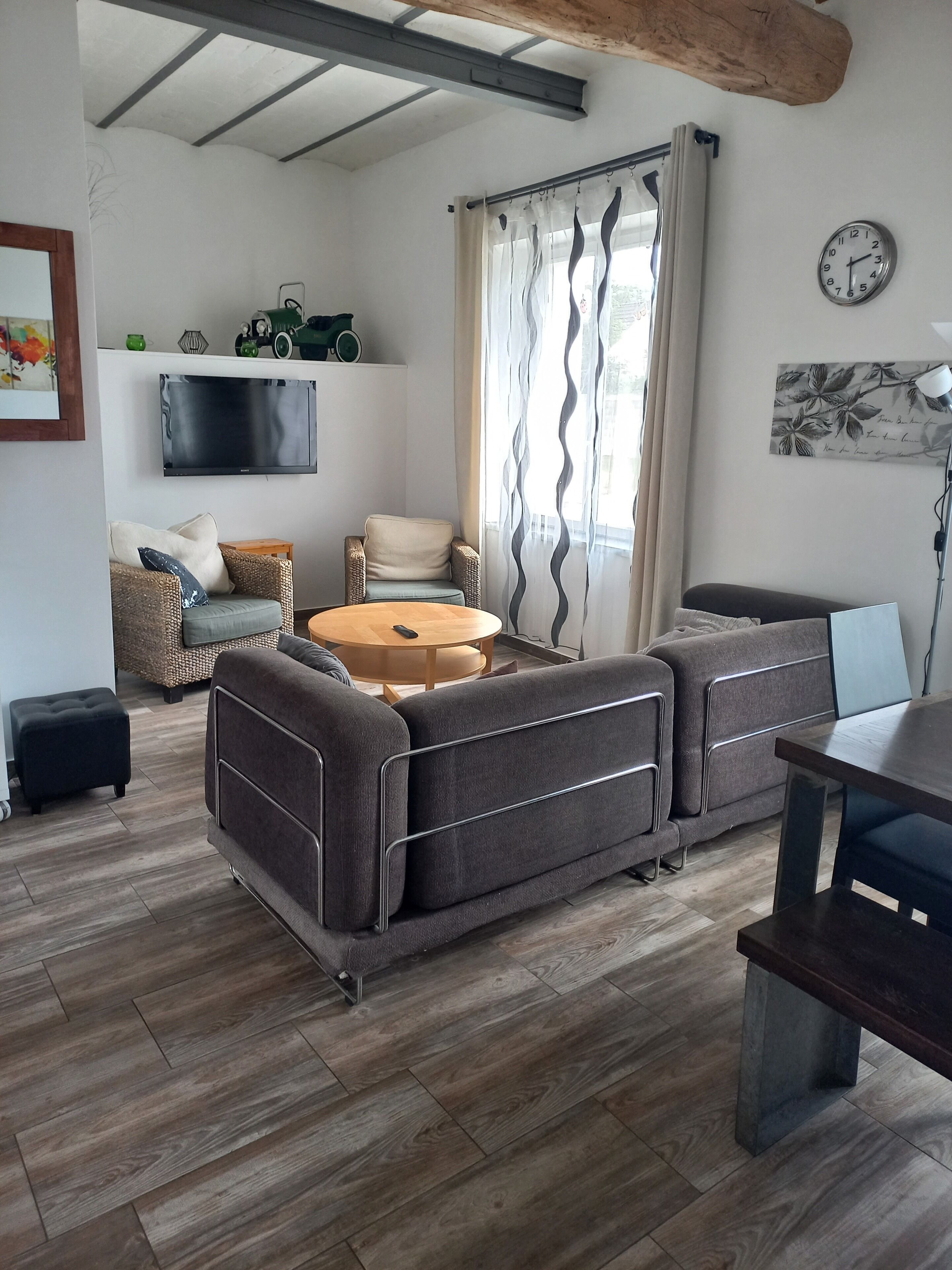 Un salon moderne avec un canapé d’angle, une table basse ronde et un téléviseur à écran plat fixé au mur.