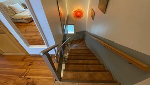 Eine Holztreppe mit Handlauf, die zu einem Zimmer mit Bett und Fenster führt.