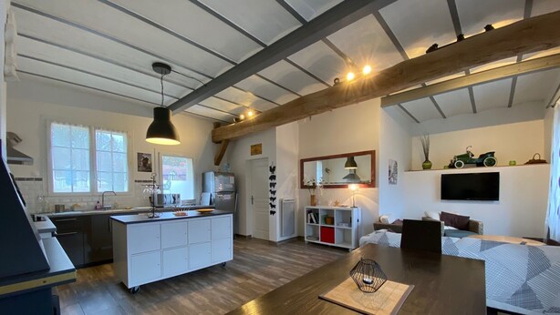 Eine moderne Küche mit einer zentralen Kochinsel, ein Essbereich mit Holztisch und ein Wohnzimmer mit Sofa und Fernseher.