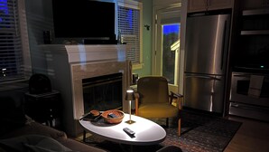 A living room with a fireplace, a television, and a kitchen area with a refrigerator and oven. - Wonderful beachside hideaway. Steps to the beach! Steps to the action! (Provincetown)