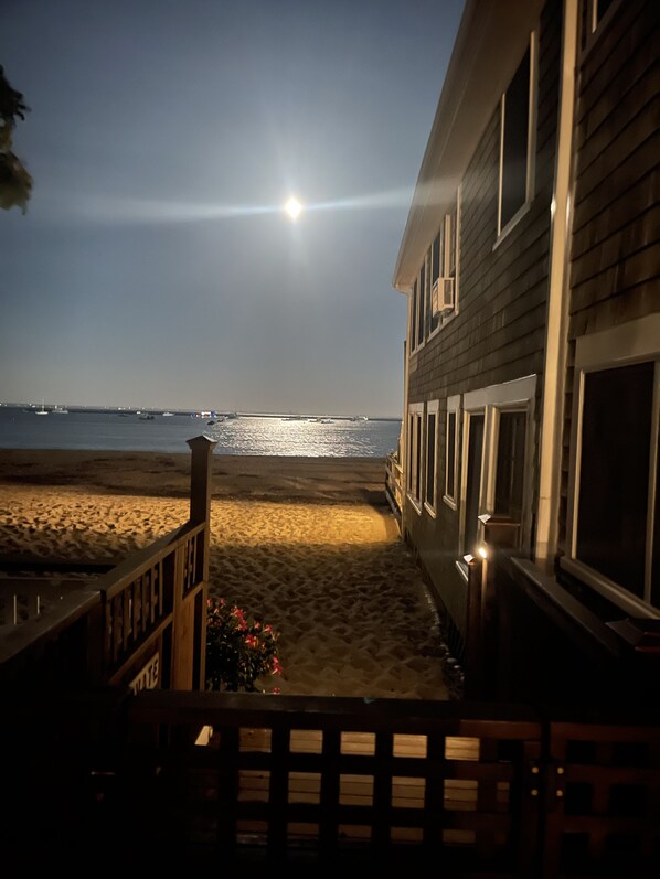 Une propriété située en bord de mer, dotée d’une terrasse en bois donnant sur une plage de sable, offrant une vue dégagée sur l’océan et comprenant un bâtiment avec de nombreuses fenêtres.