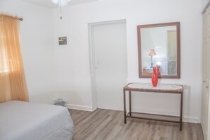 A bedroom with a bed, a bedside table with a vase, a mirror, and a door. - Private Duplex Near MIA & Port (Miami)