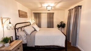 Una cama bien hecha con una colcha a rayas, una lámpara de noche y una planta pequeña sobre una mesita de madera.