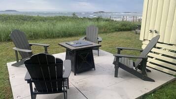 Une terrasse extérieure avec des fauteuils Adirondack et une table, donnant sur une plage et offrant une vue sur des îles lointaines.