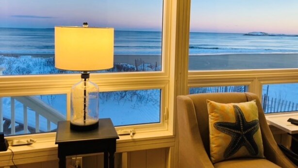 A room with a view of the ocean, a lamp on a table, and a starfish pillow on a sofa. - Popham Beach Direct Oceanfront Cottage Steps to the sand (Phippsburg)